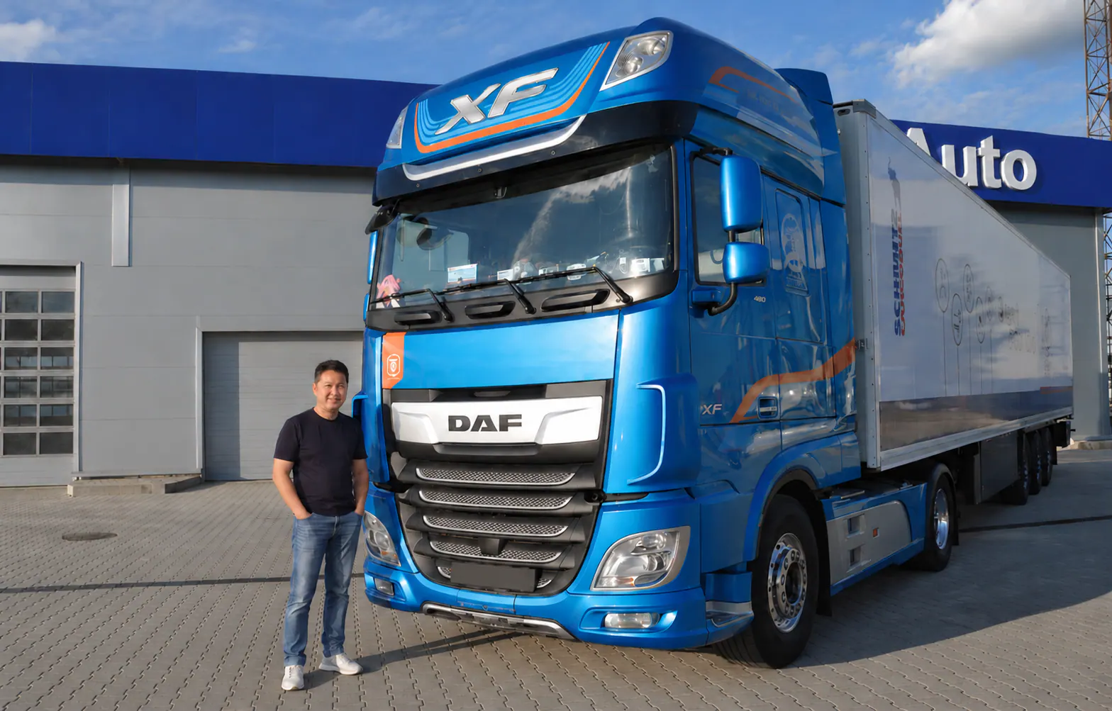 Синий седельный тягач DAF XF с полуприцепом и сотрудник компании рядом